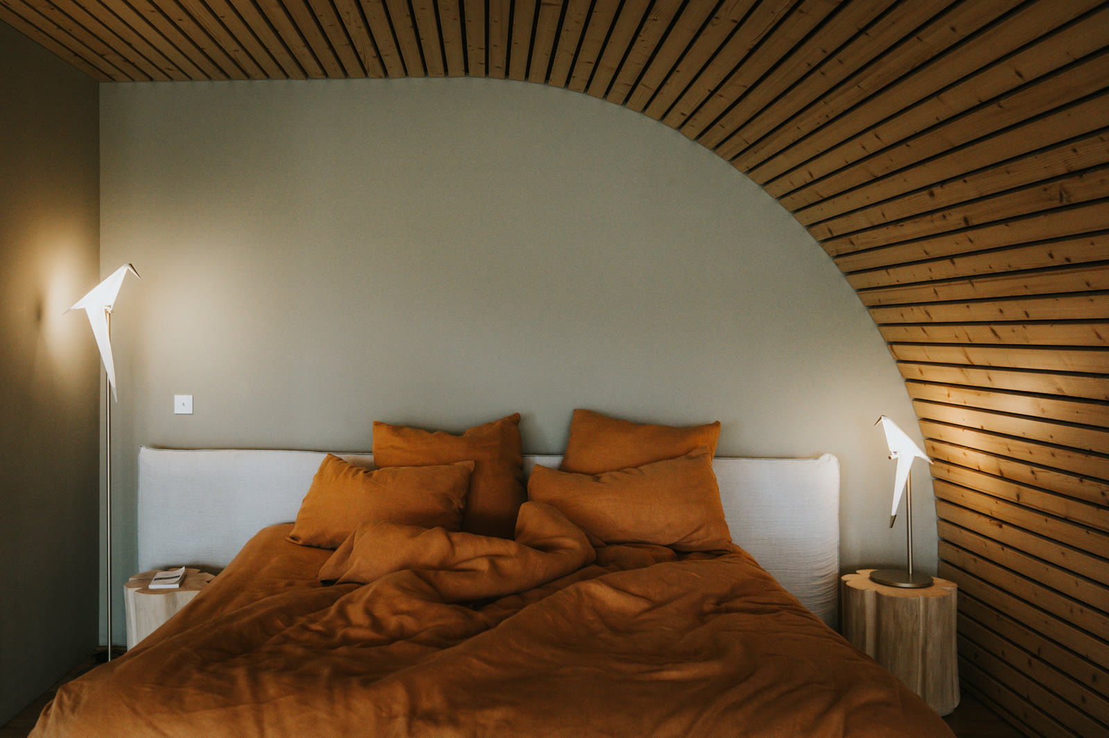 Lit d'un lodge Souki en octobre, draps de lin terracotta, deux appliques allumées sous la voûte de bois