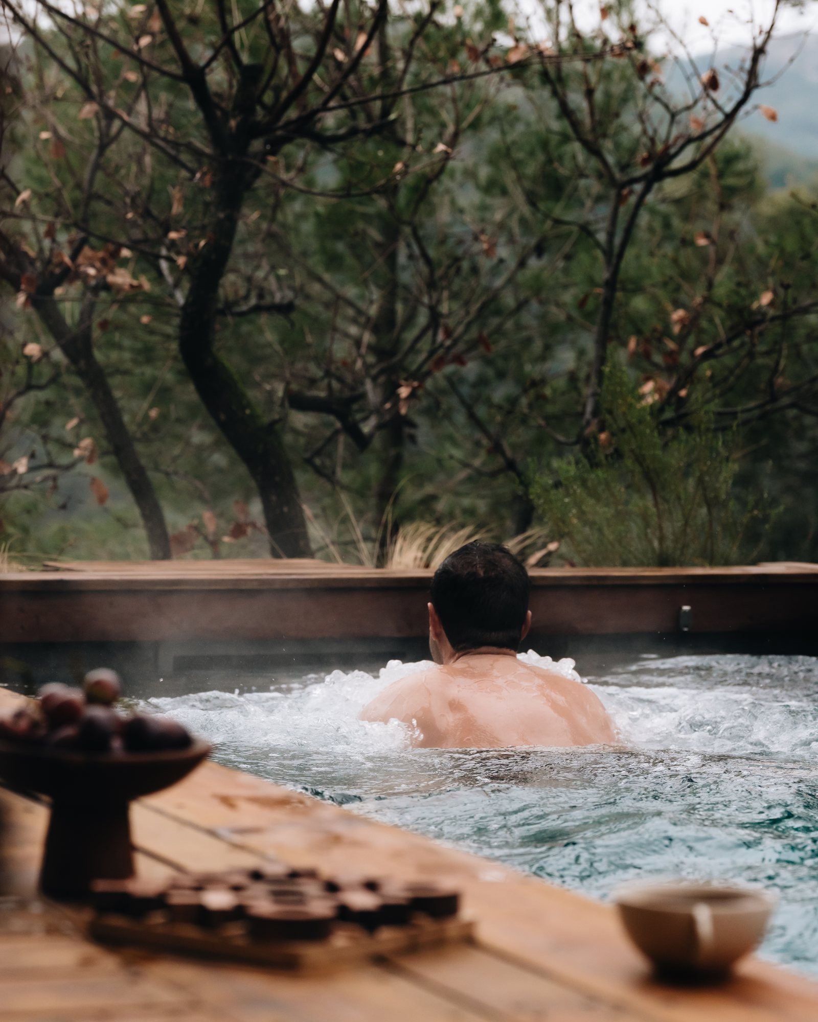 Un baigneur de dos dans la piscine privée chauffée d'un lodge Souki, la vapeur au-dessus de l'eau et les branches nues de l'arrière-saison