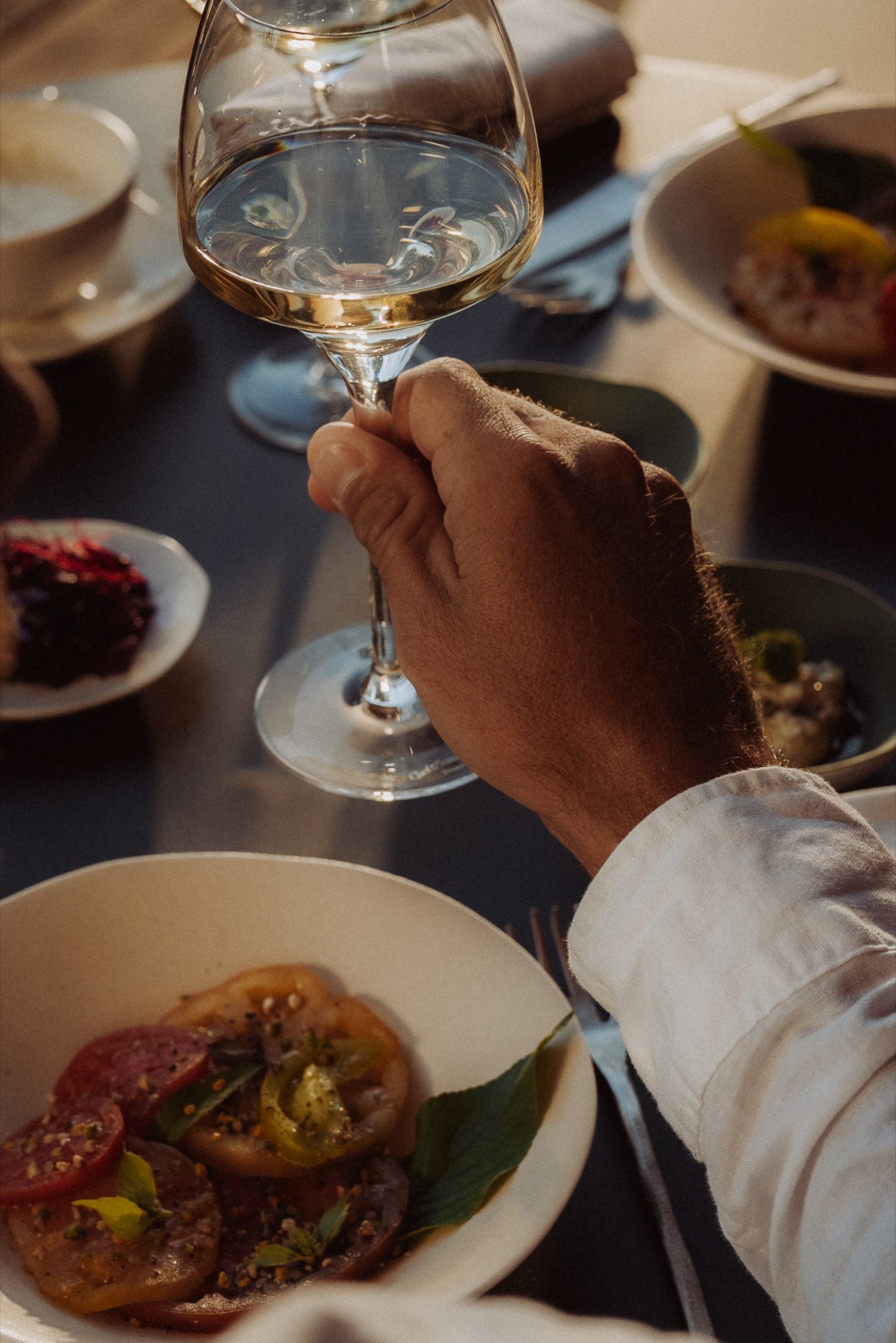 A glass of white wine raised above a Menu Balade plate, in a Souki lodge