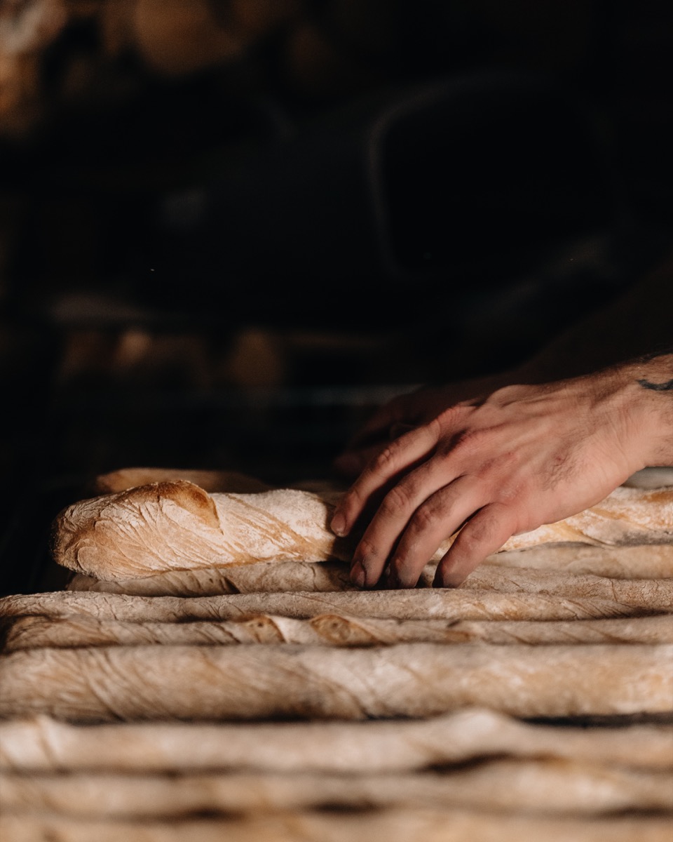 Des baguettes cuites alignées, une main posée dessus à la sortie du four