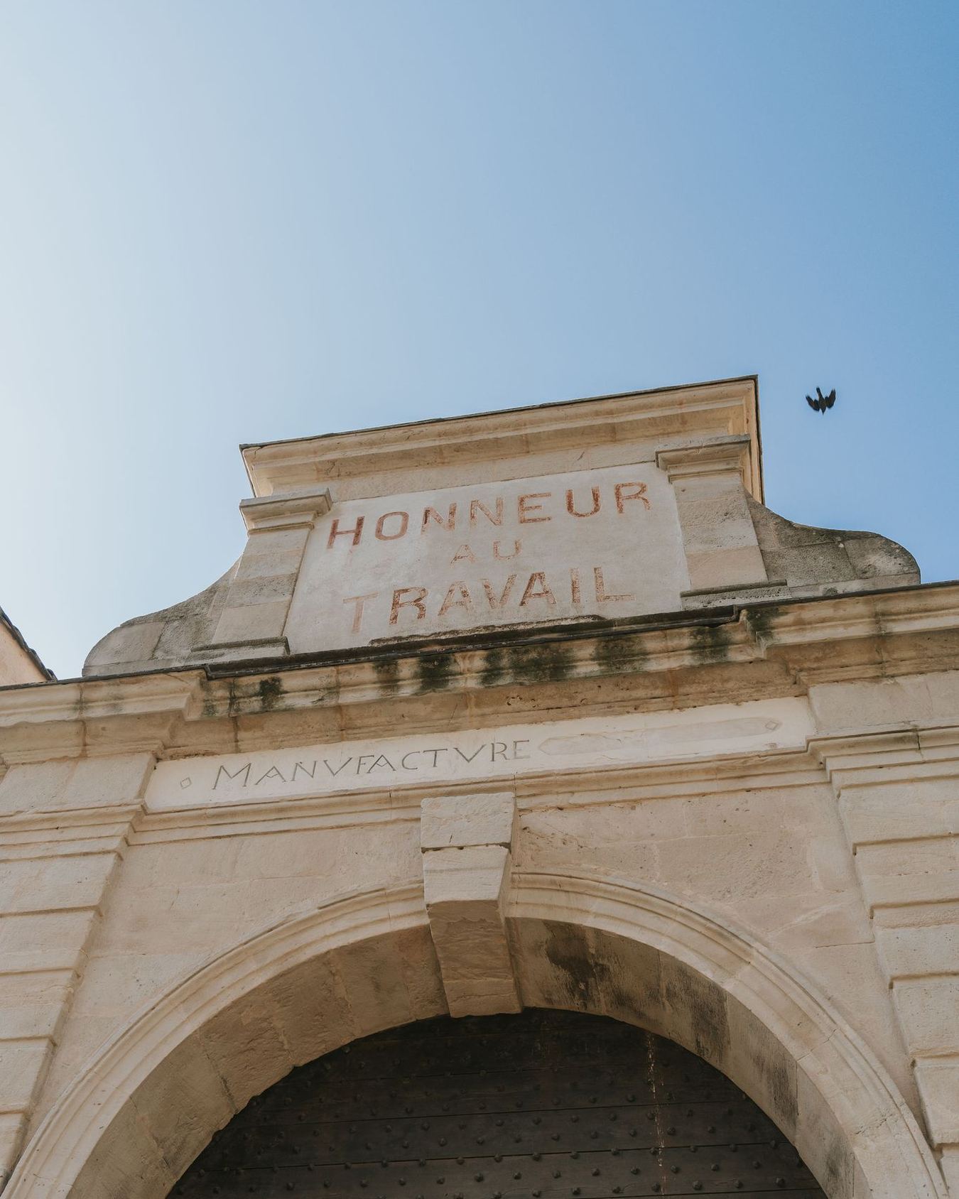 The gate of the Villeneuvette manufactory, “Honneur au travail” carved into the pediment above the arch