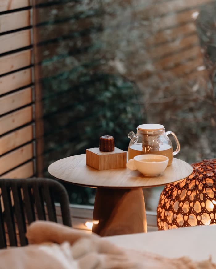 Une théière et deux tasses sur la table ronde de la terrasse, une lampe allumée dans la pénombre