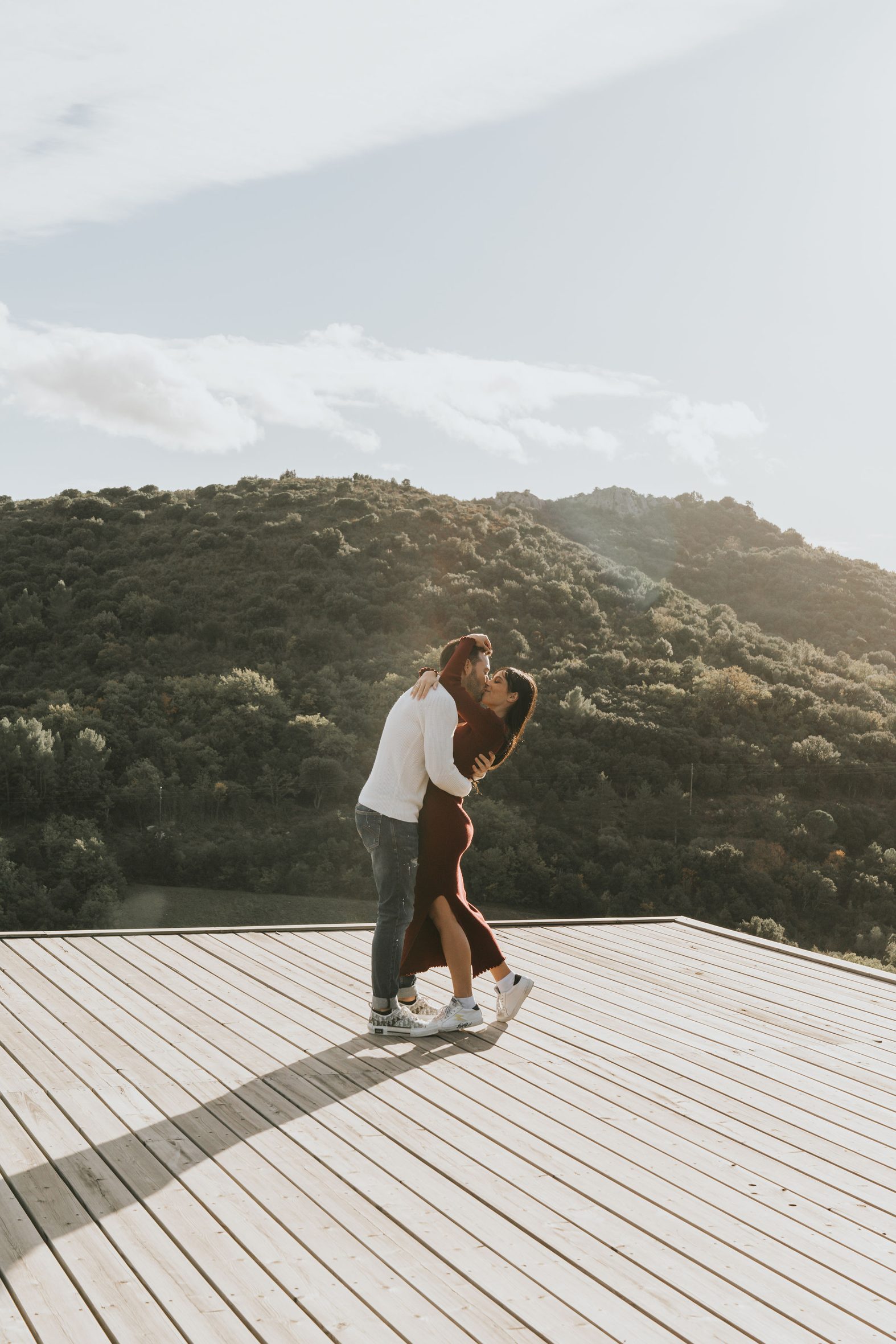 Couple embracing on the terrace of a lodge against the light, the scrubland hills behind, Souki Lodges & Spa
