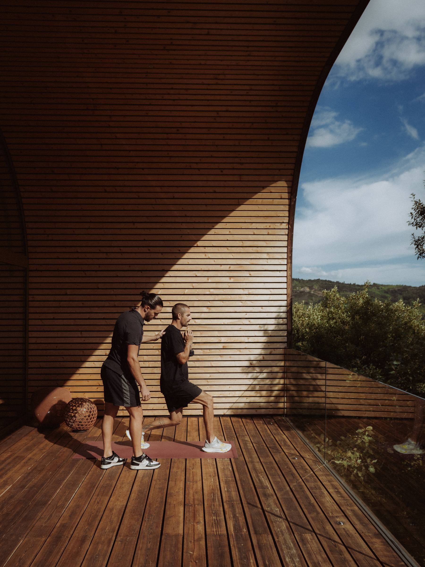 Lunges along the wooden wall of the terrace, the coach accompanies the movement