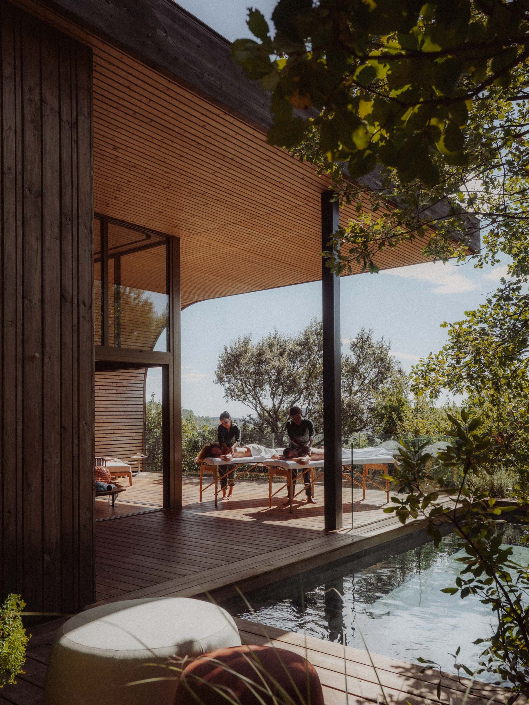 Two massage tables installed on the terrace at the edge of the pool, seen through the foliage of the oak trees