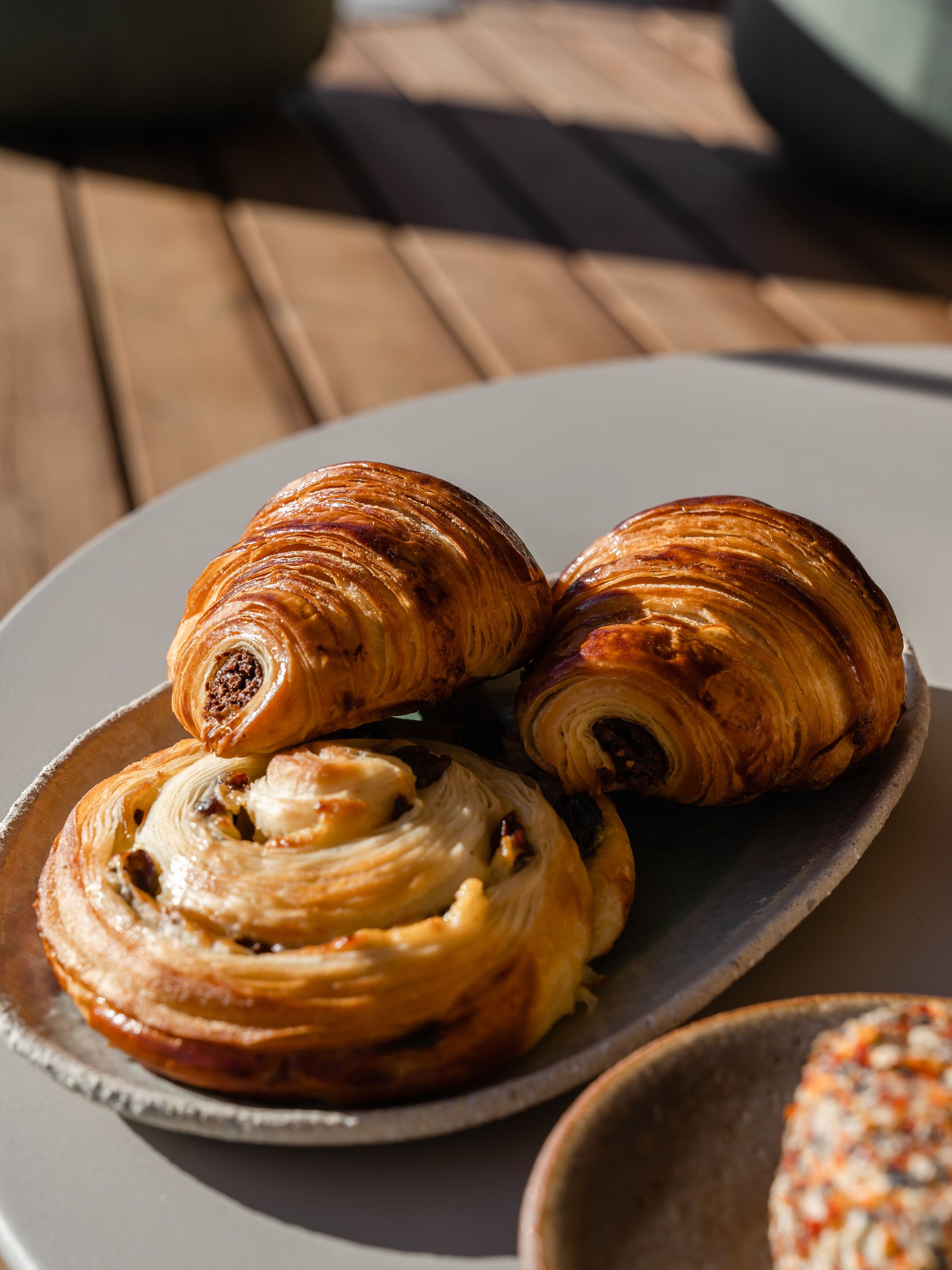 Close up: pains au chocolat and a raisin swirl on a plate, in full light