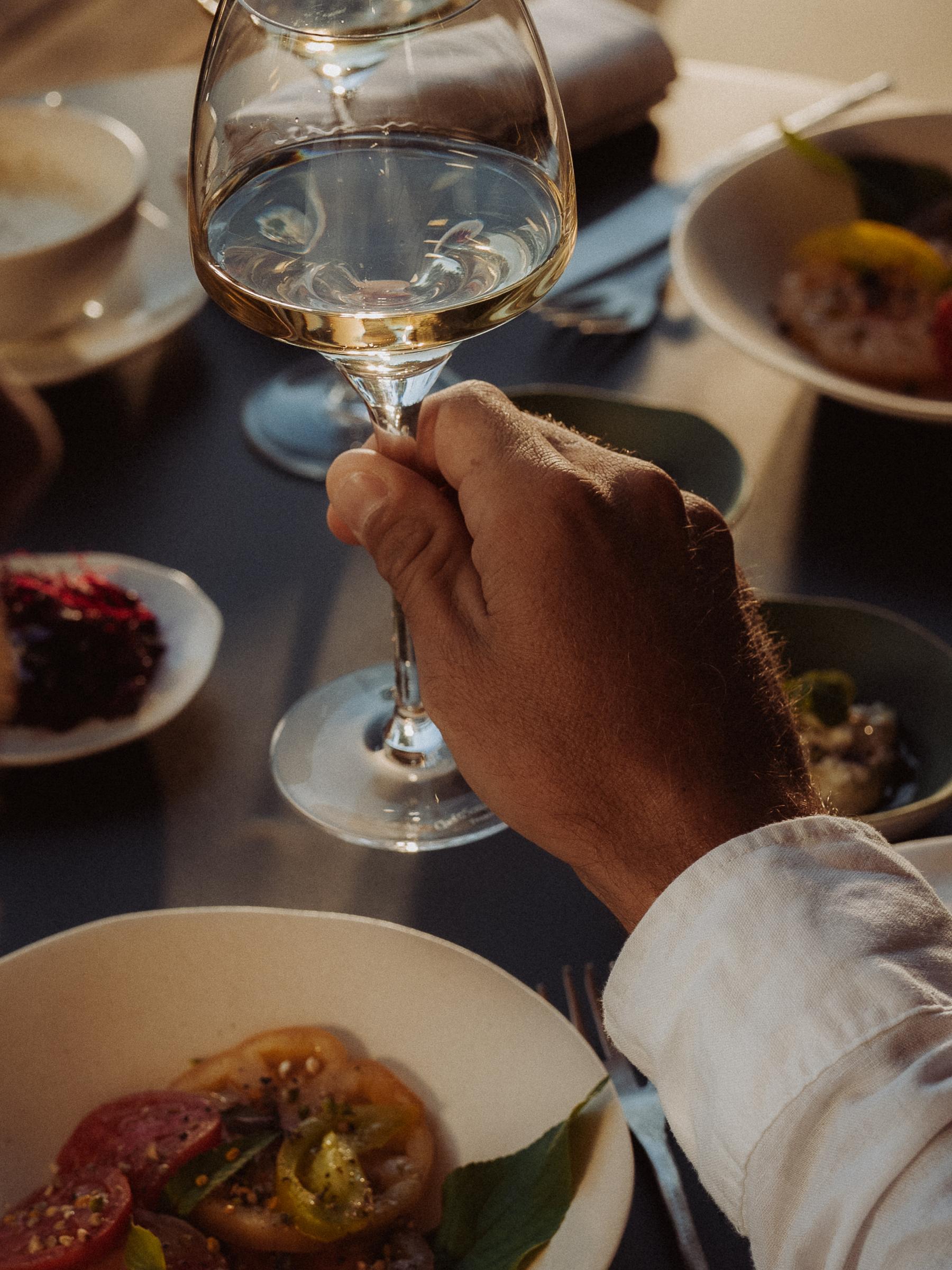 Evening table: a hand raises a glass of white wine above the plates